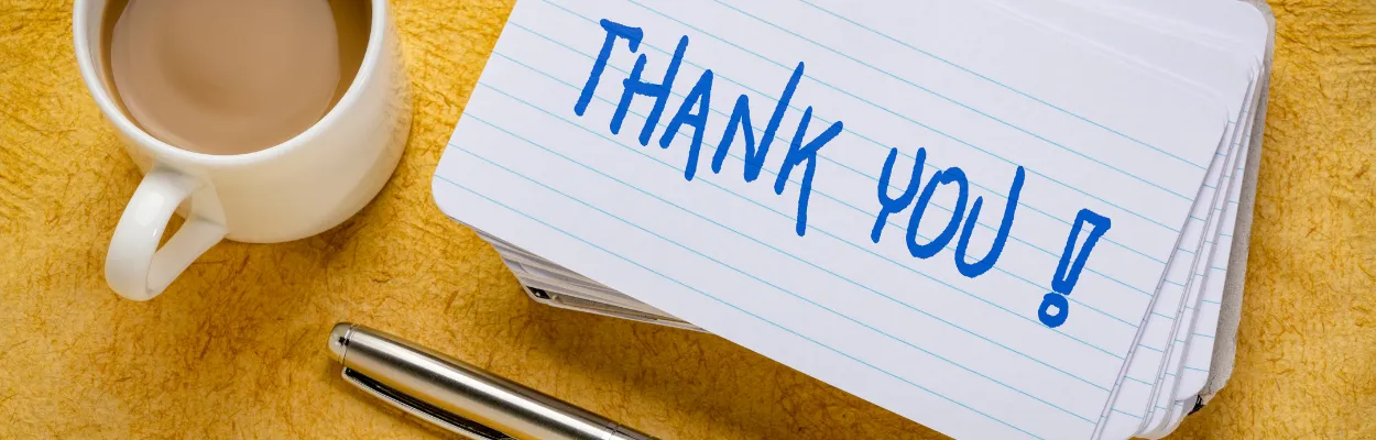 Kartka z napisem thank you, kubek z kawą i długopis na blacie biurka 